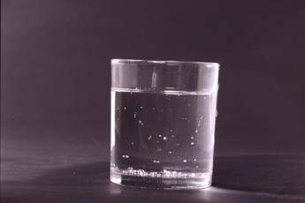 Clear glass of water on a dark surface with a few bubbles in the water or at the bottom surface a shallow reflection of light.