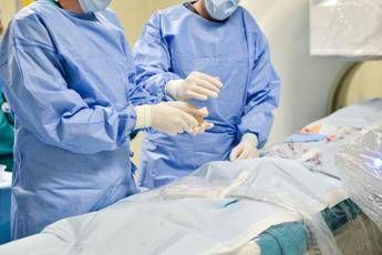 Two surgeons in blue scrubs and masks perform a procedure on a patient in an operating room.