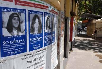 Row of blue and white missing-person posters with portraits along a sunlit street wall.