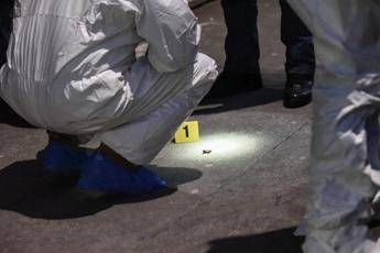 Forensic investigators in protective suits examine a white body bag at a crime scene, with a yellow evidence marker labeled 1 on the ground.