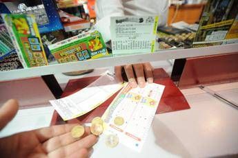 Customer at a checkout counter holds coins and receipts while placing them on the counter near a cash register in a store.