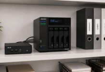 Micro-Datacenter ASUS e ASUSTOR: sovranità digitale e risparmio per le micro imprese italiane NAS server with multiple drive bays on a shelf, connected to a small network box, next to labeled binders and a plant.