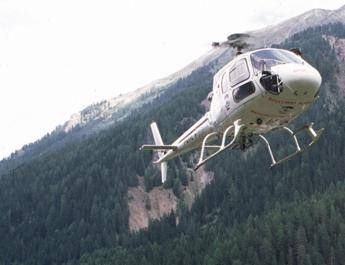 White helicopter in flight above a dense forest on a mountainside mountain slope